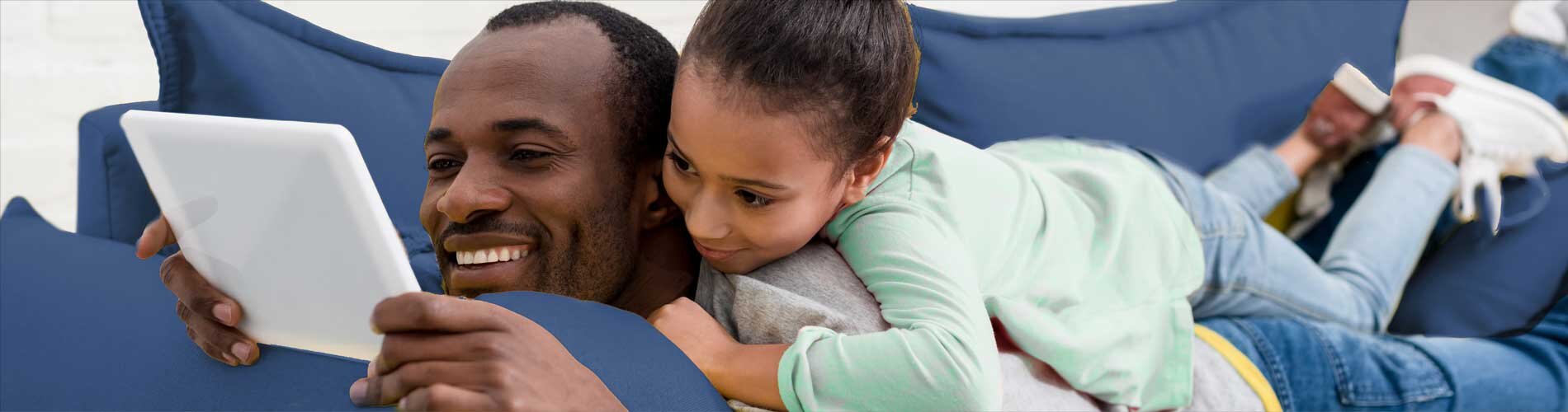 Small child laying on fathers back looking at tablet together